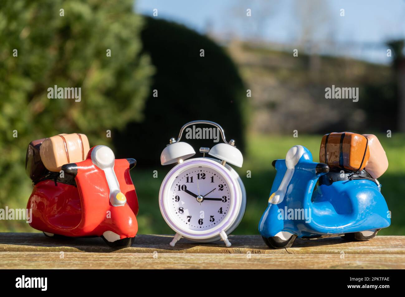 Time has come for travel, delivery concept. Two toy scooters and outdoor alarm clock. Stock Photo