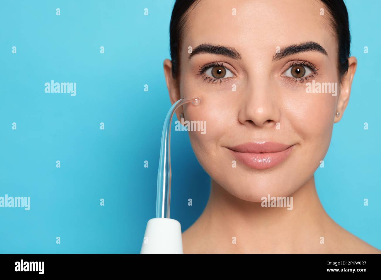 Woman using high frequency darsonval device on light blue background ...