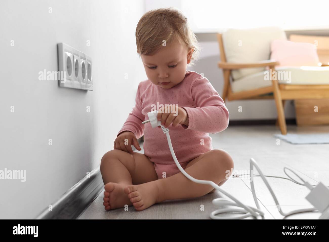Cute baby playing with plug at home. Dangerous situation Stock Photo