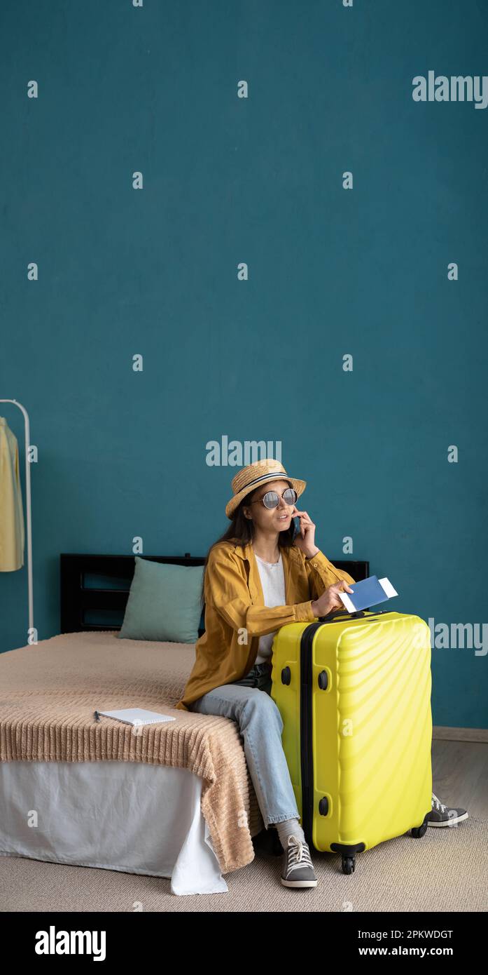 Woman traveler talking on mobile phone, sitting on bed at suitcase calling a taxi calls, waiting for transport to the airport, she sits with baggage i Stock Photo