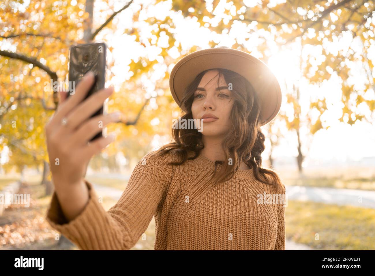 Beautiful dreamy lady make selfies wearing hat walking in autumn park, enjoying warm day. Copy space Stock Photo