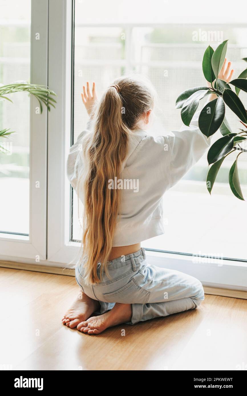 Lonely sad little girl sitting by the window. Stock Photo