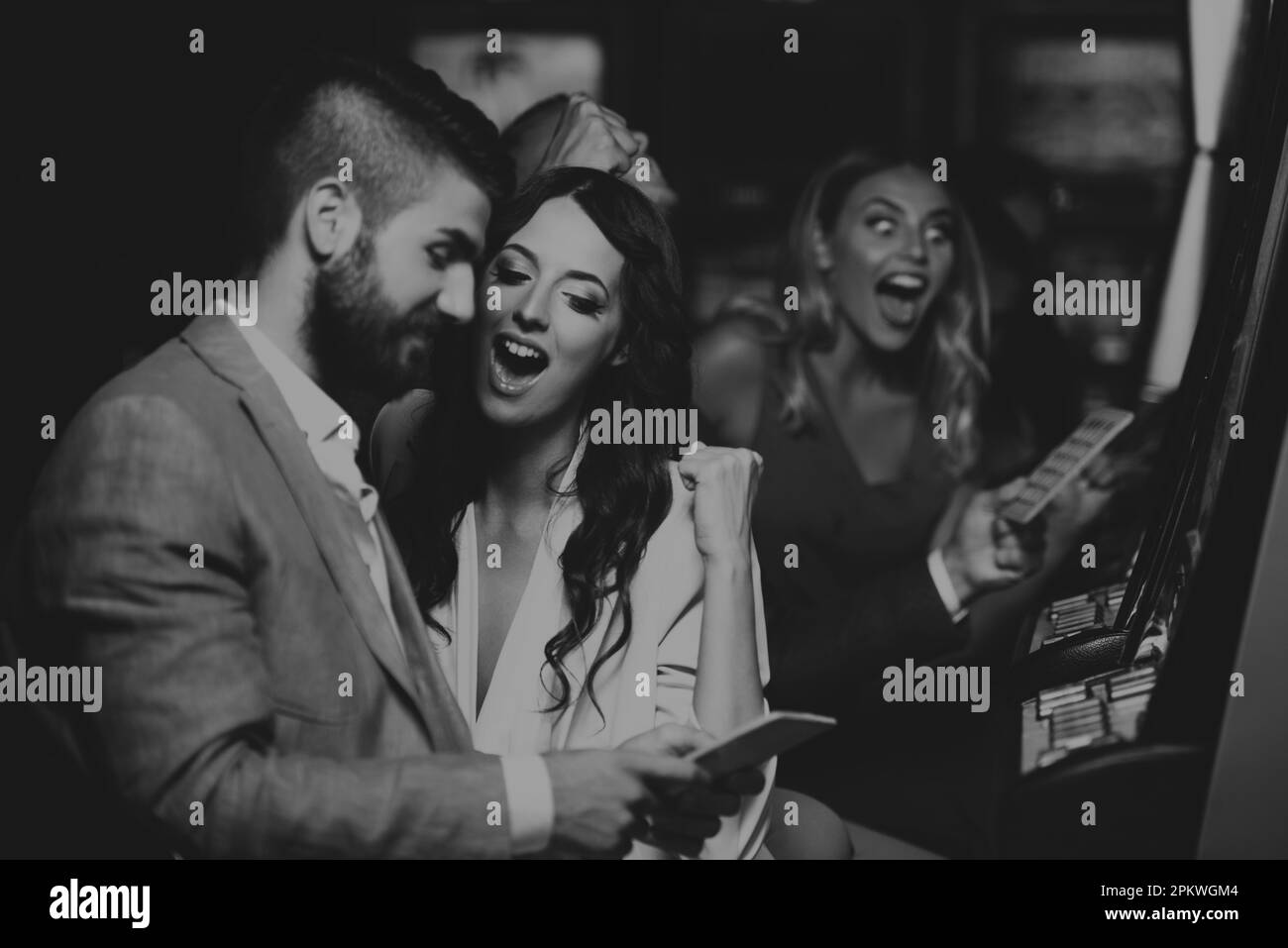 Beautiful and Well Dressed Friends Playing Automat Machine in the Casino and Celebrate Stock Photo
