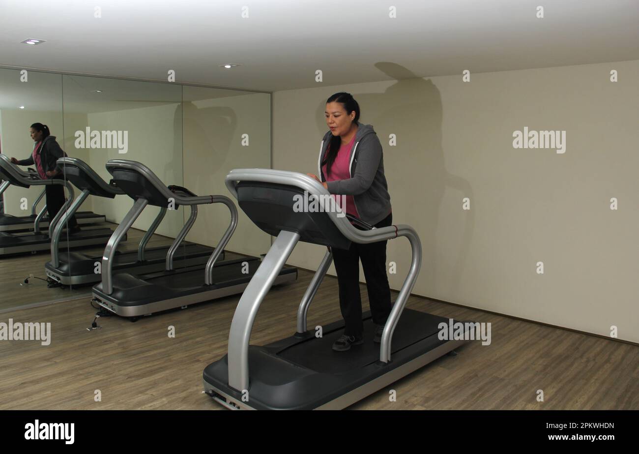 Latino adult woman exercises on treadmill in gym to relax and avoid