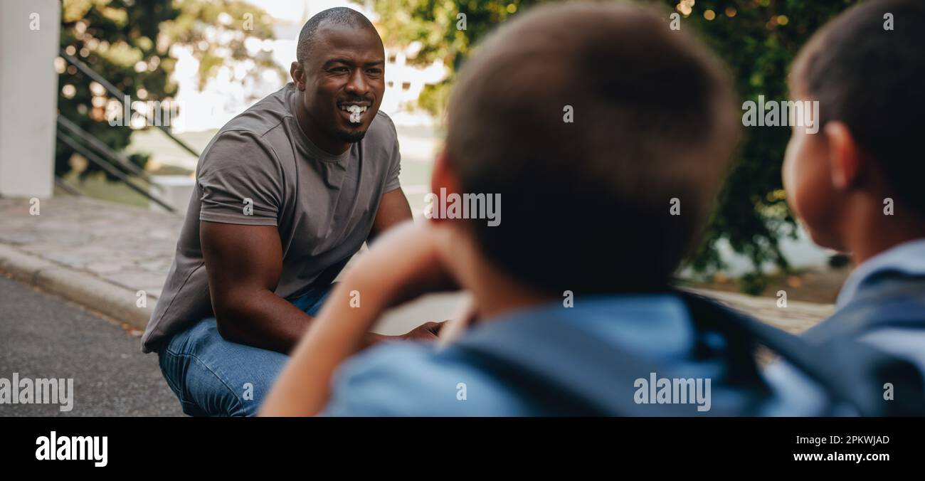 Teacher giving his students a pep talk in elementary school. Male educator motivating a group of children before class. Mentorship and guidance in pri Stock Photo
