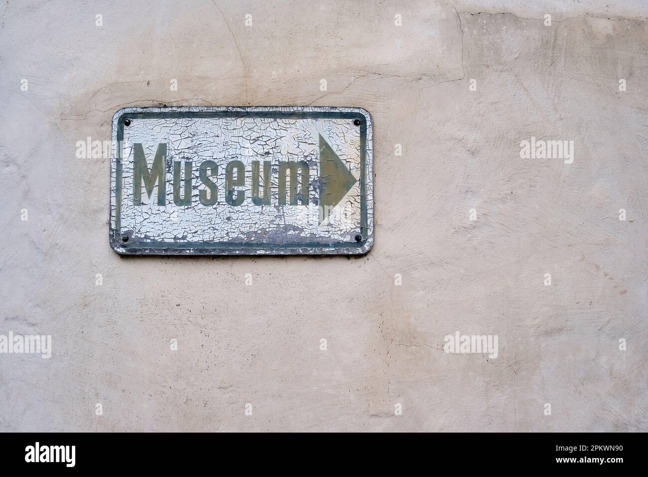 Yellowed and weathered sign full of cracked paint with a directional label saying MUSEUM painted on it. Stock Photo