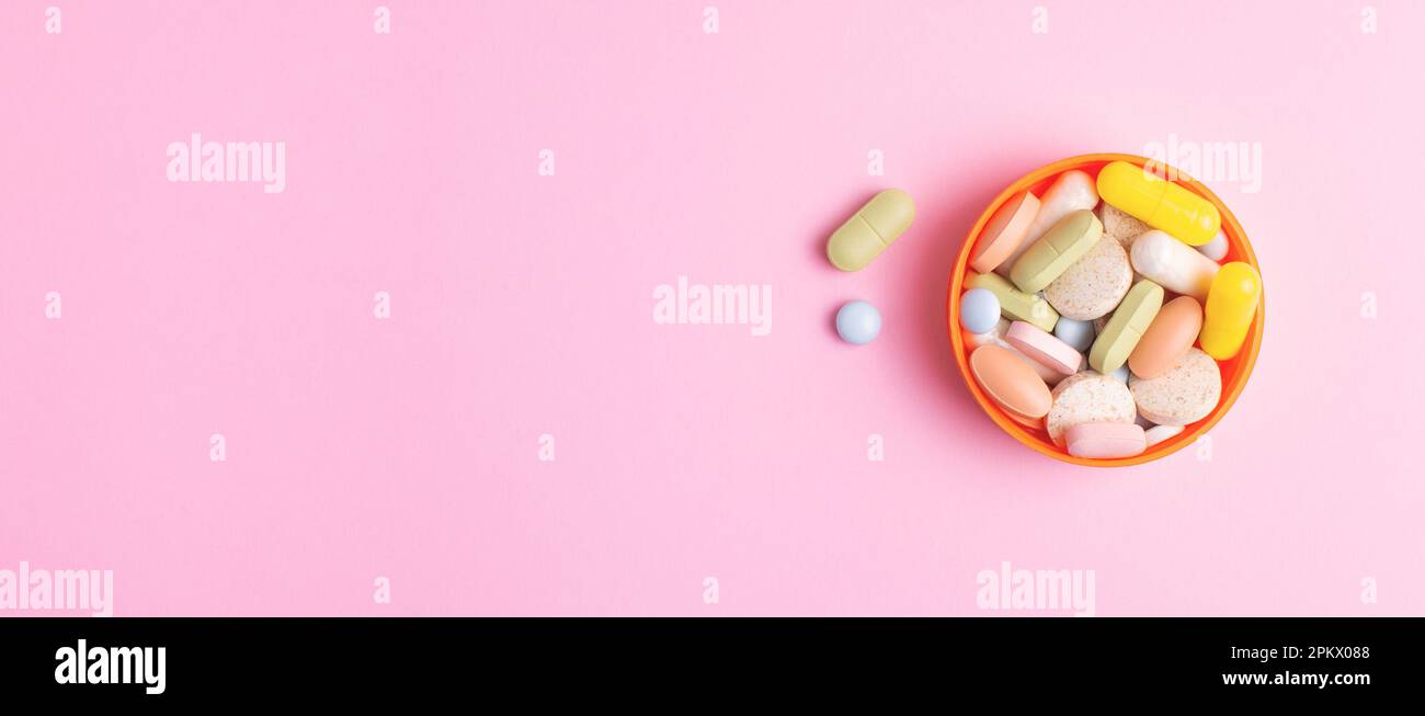 Colourful pills, capsules, vitamins and dietary supplements of different shape, size and color in a bowl isolated on pink background. Web banner. Stock Photo