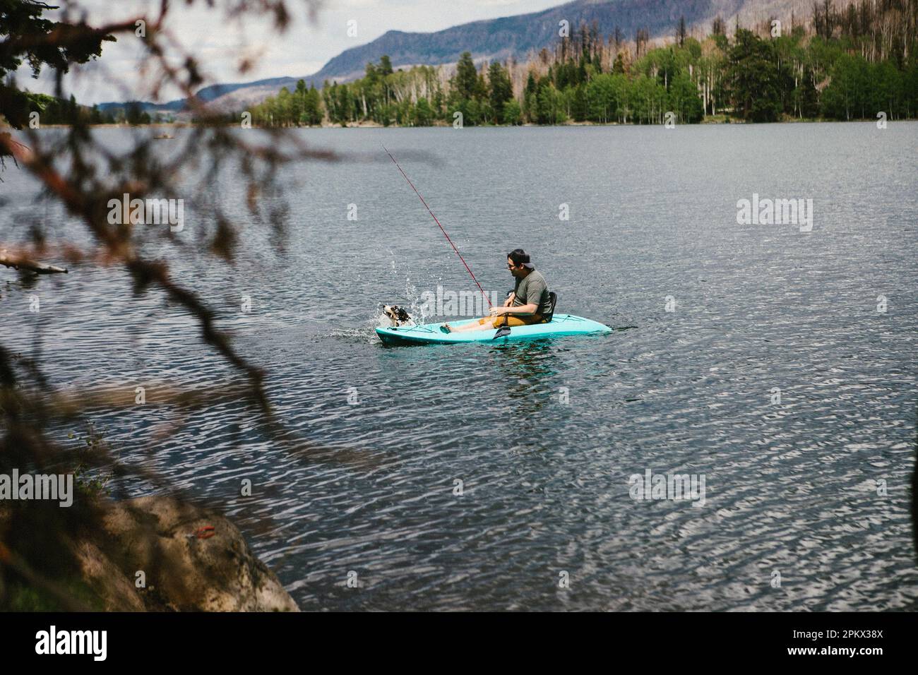 Man fishing in a kayak on a lake in mountains with dog Stock Photo