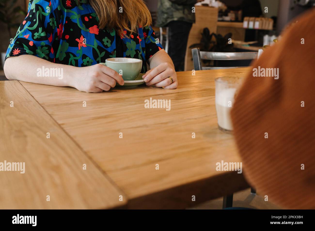 Two people’s hands & coffee mugs while sitting at table Stock Photo