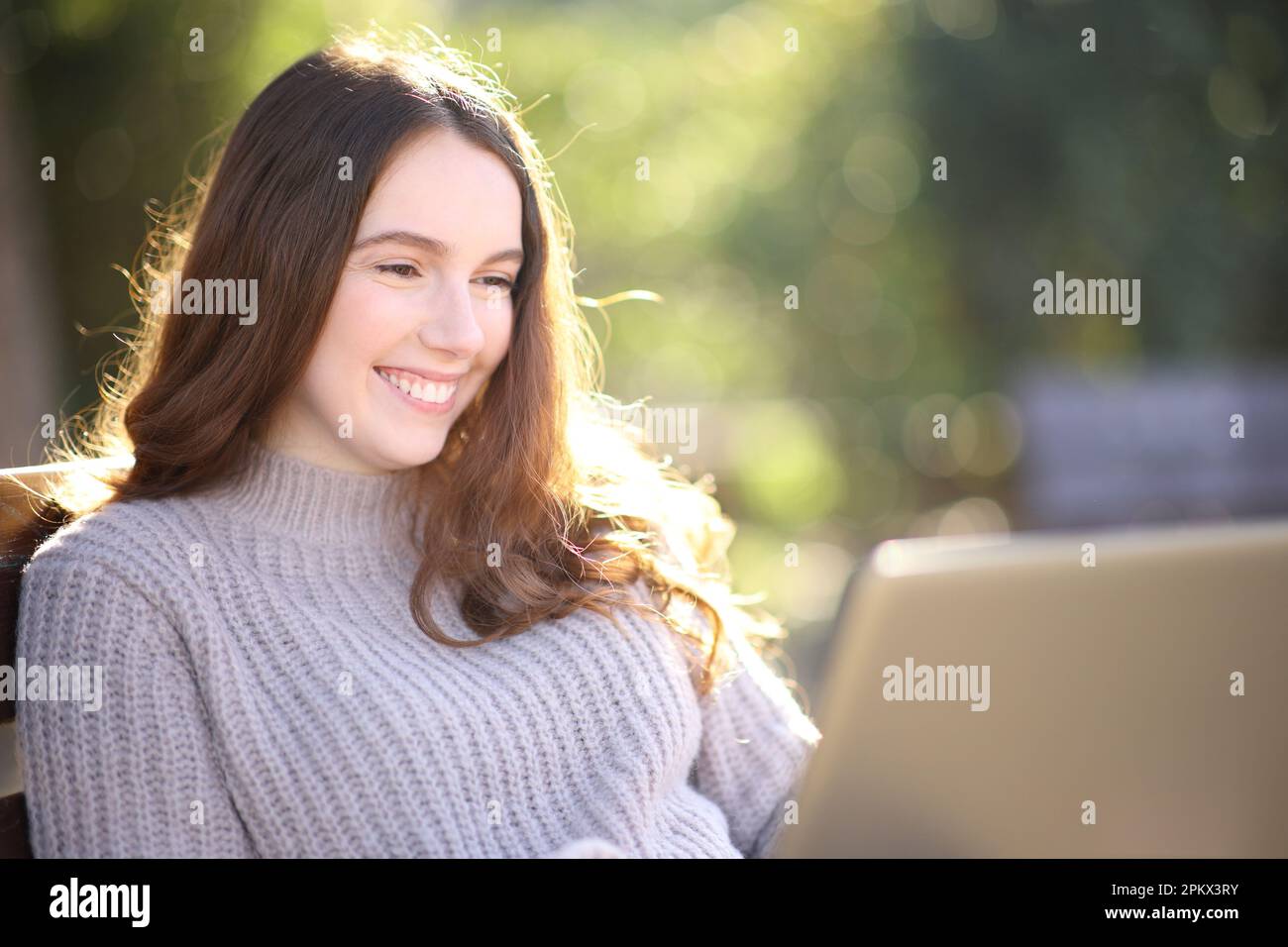 Happy woman is using laptop sitting on a bench in a park Stock Photo
