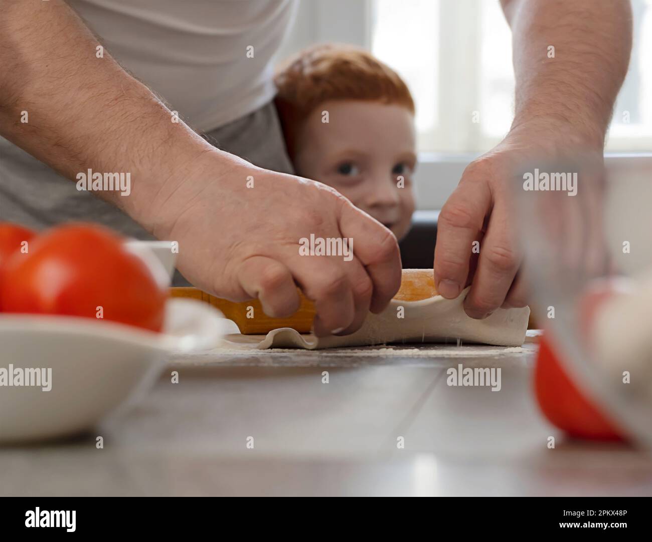 Male hands roll out the dough, the baby looks out. Stock Photo