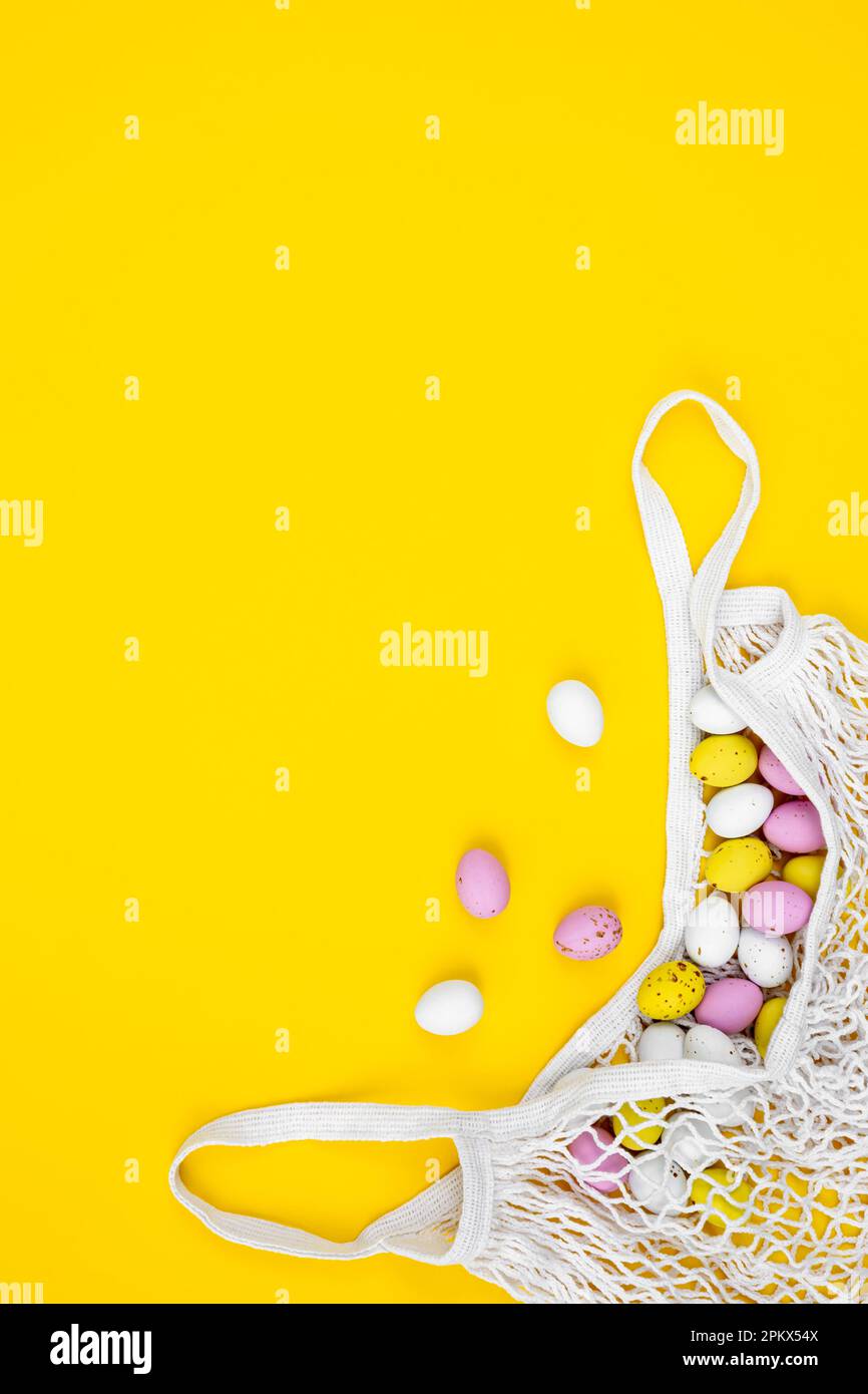 Colored Easter eggs in a mesh bag on a yellow background, flat lay. Stock Photo