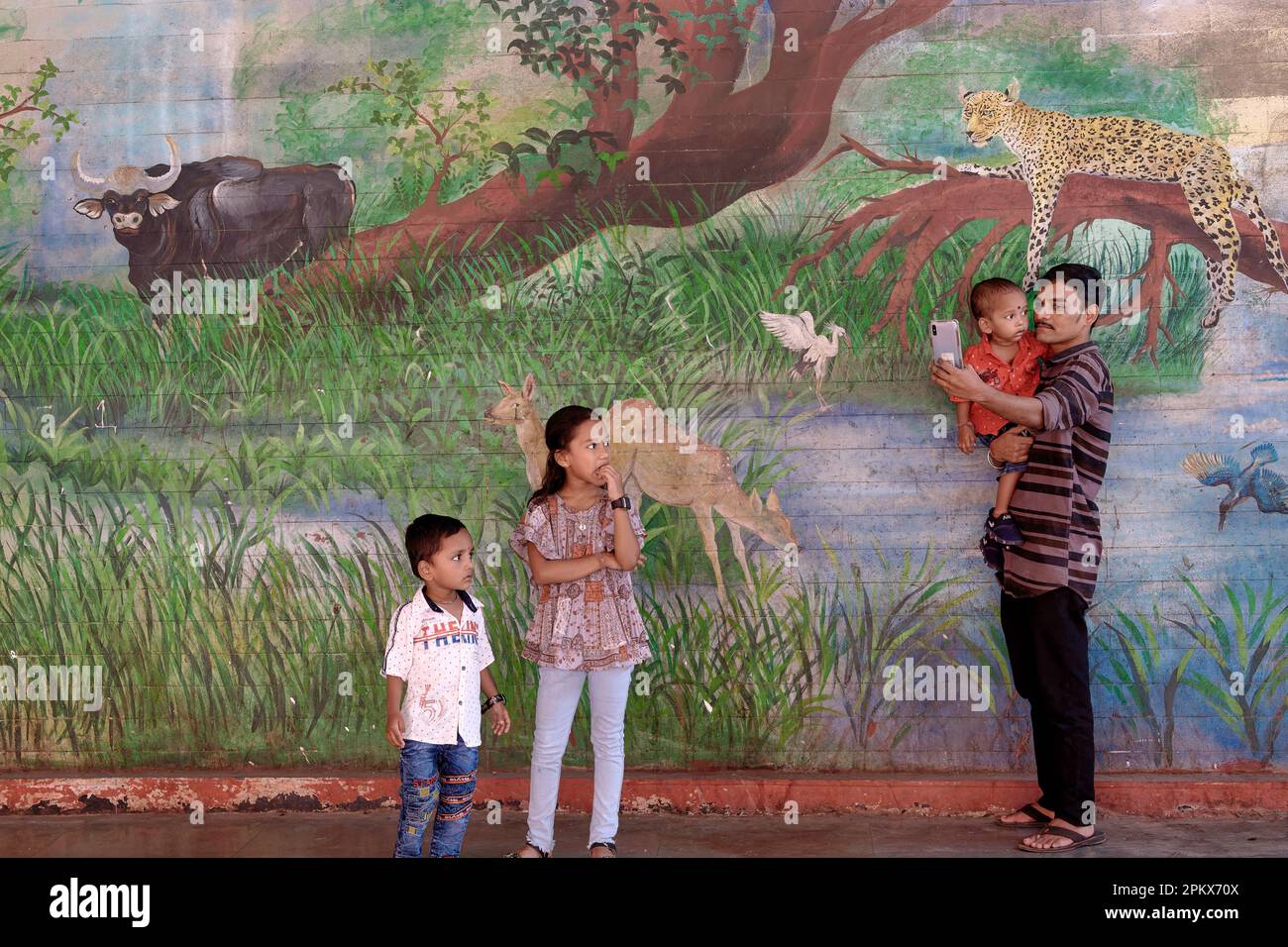 A father takes selfies with his children at a mural at Byculla Station in Mumbai, India, its wildlife theme a homage towards the nearby Byculla Zoo Stock Photo