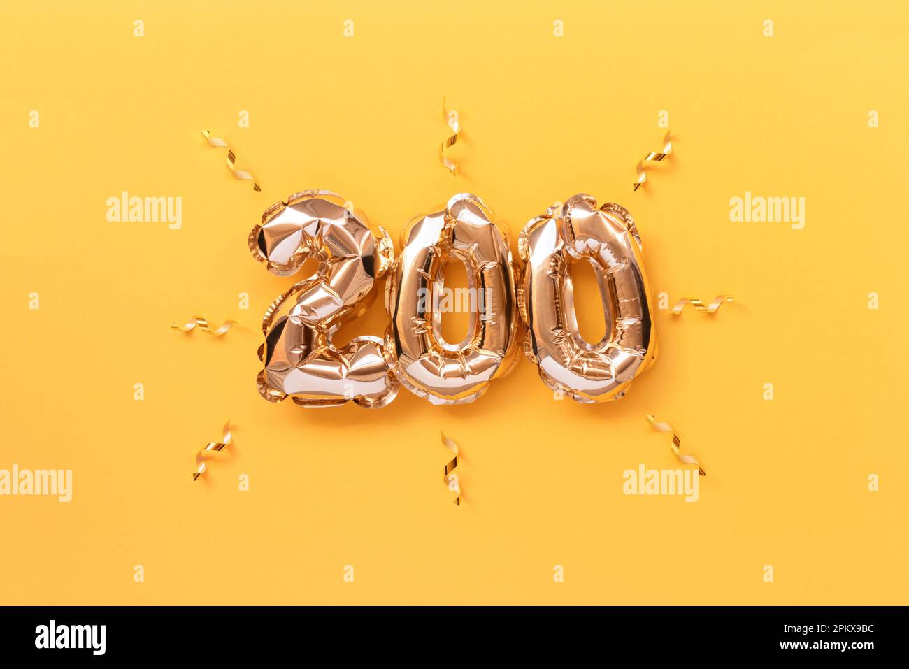 Number 200 golden air balloons with ribbons confetti on a yellow background. Stock Photo
