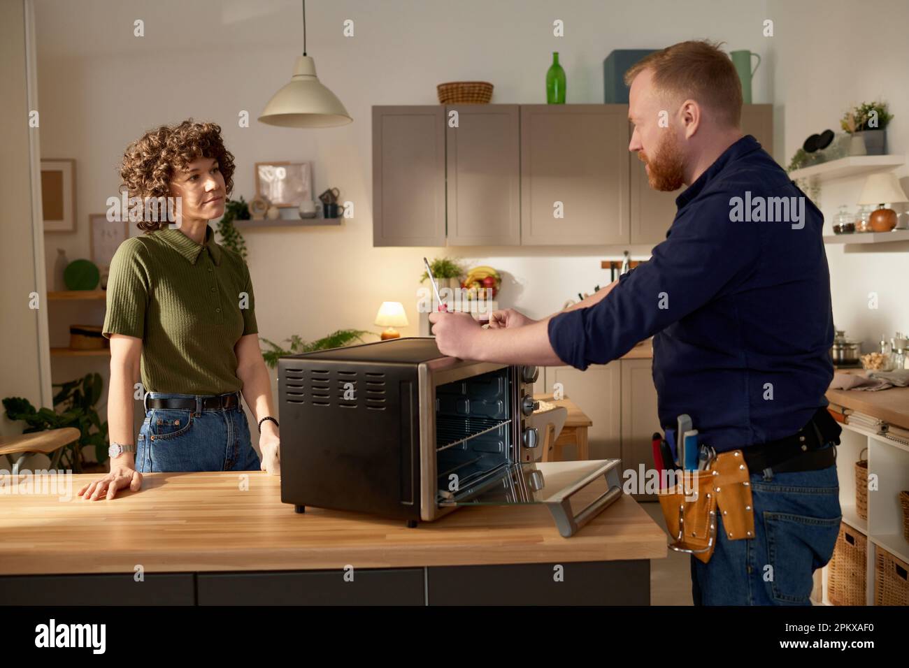 Professional serviceman repairing broken microwave oven and talking to