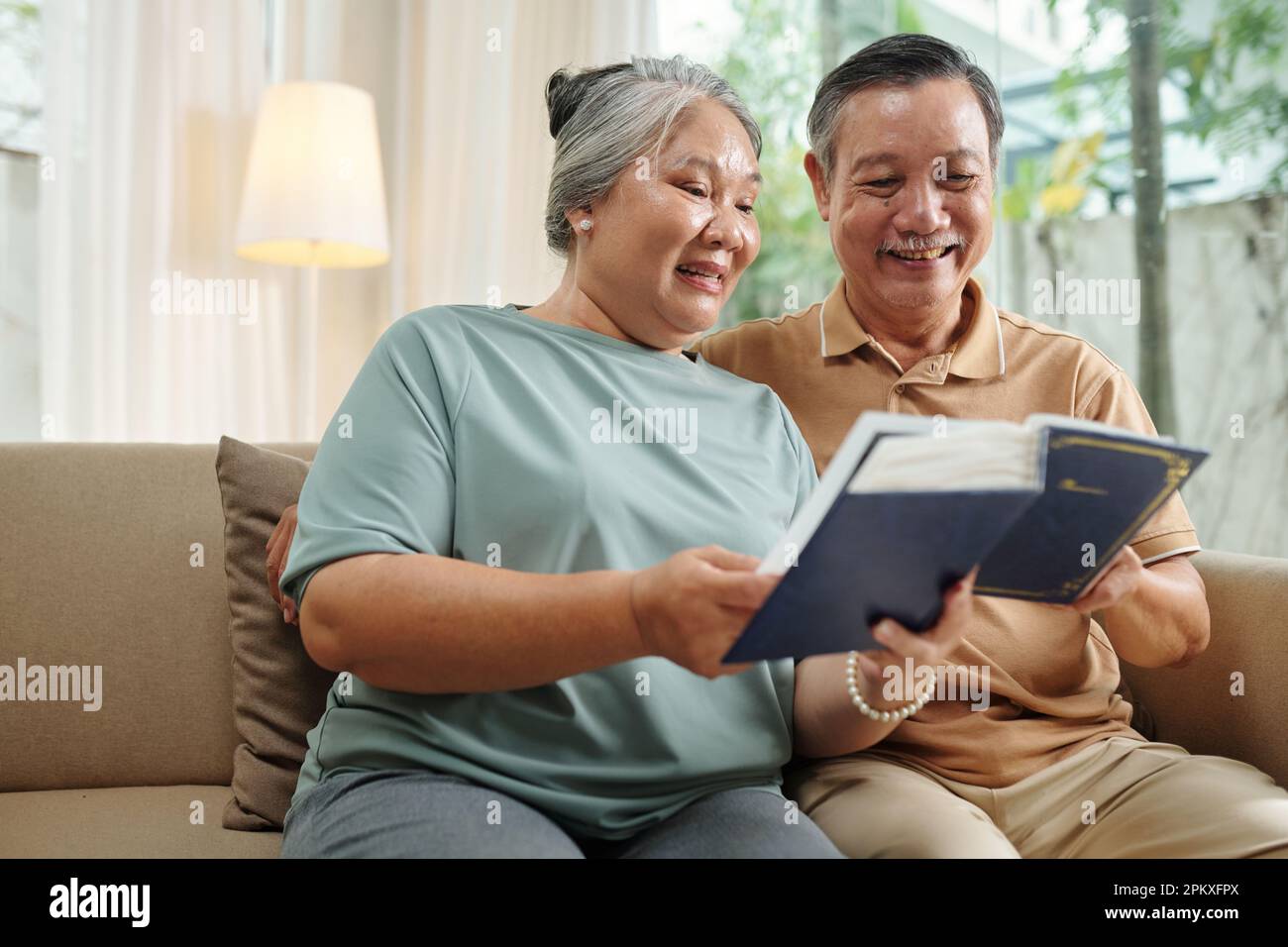 Senior couple looking at old photos in album when resting on couch at ...