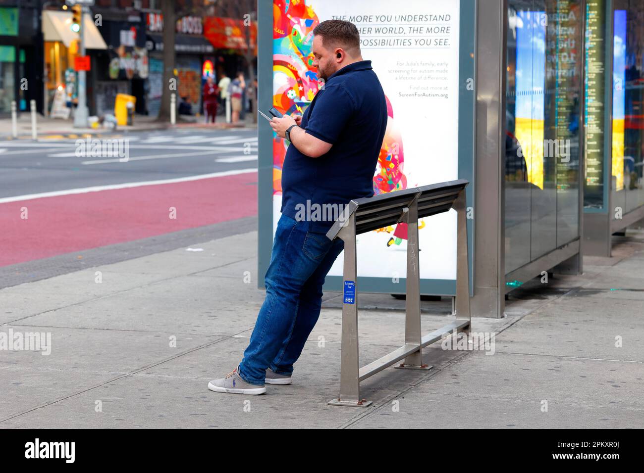 A person resting against a leaning bar, or leaning bench at a Manhattan bus stop in New York City. Hostile architecture against sitting and loitering. Stock Photo