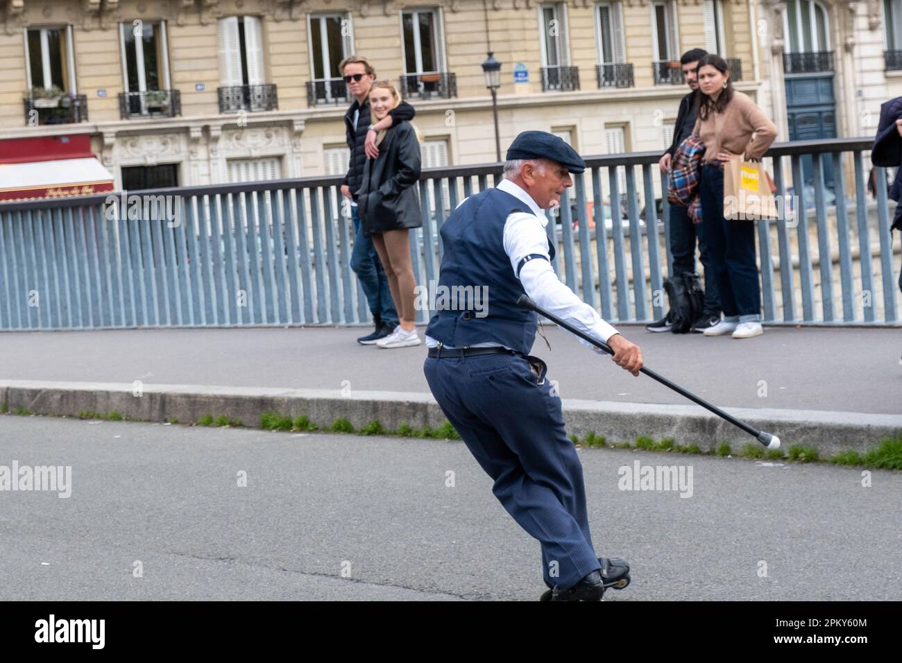 Timeless Showmanship: 60-Year-Old Man in 1940s Attire Executes Impressive Roller Blade Tricks on a Parisian Bridge, Captivating the Onlookers Stock Photo