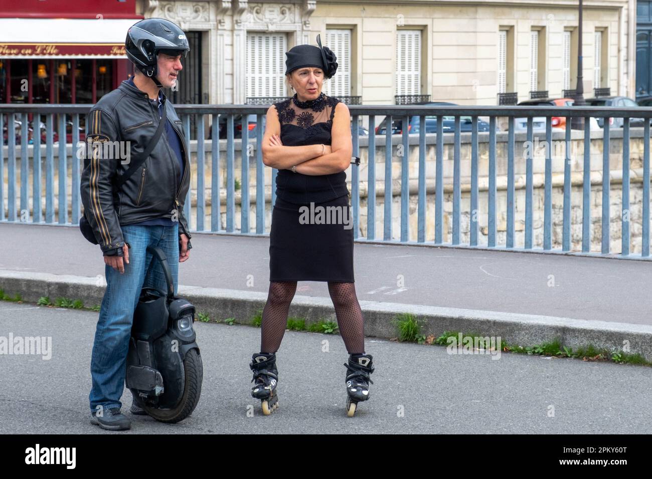 Timeless Encounters: 60-Year-Old Woman on Roller Blades in Vintage 1940s Attire Conversing with White-Bearded Man on Electric Unicycle Stock Photo