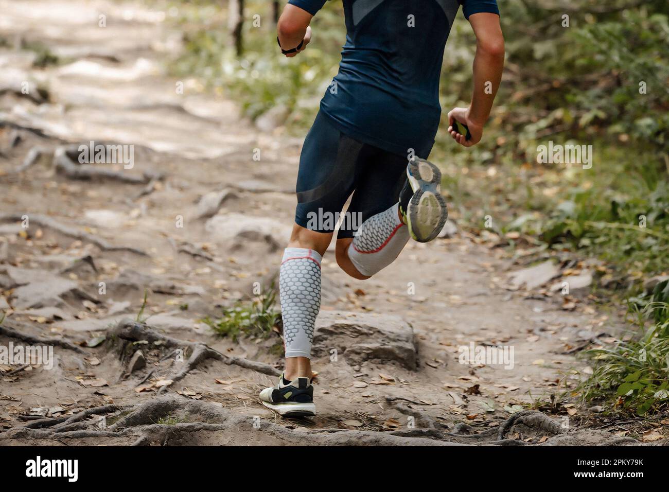 back athlete runner in compression sleeves on his feet running forest trail, summer marathon race Stock Photo