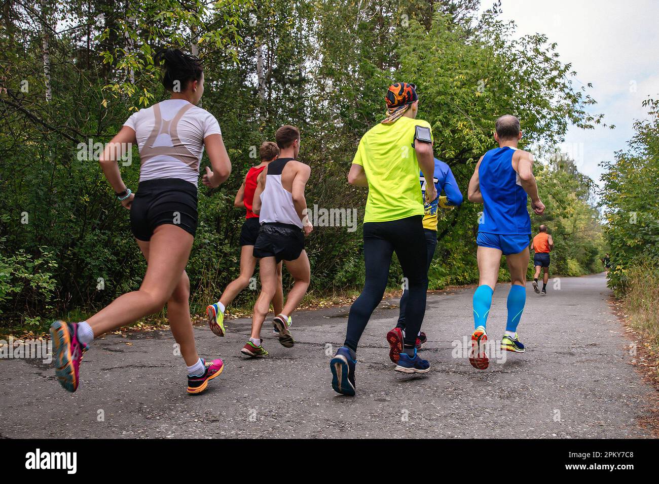 group runners male and female running race on park road rear view