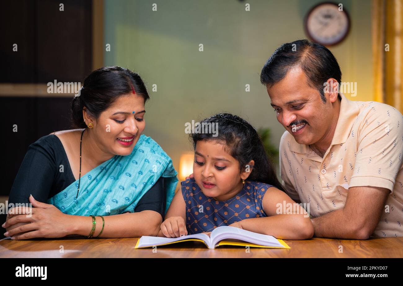 Couple got happy by seeing little girl daughter confidently reading book at home - concept of intelligence, family caring and education Stock Photo