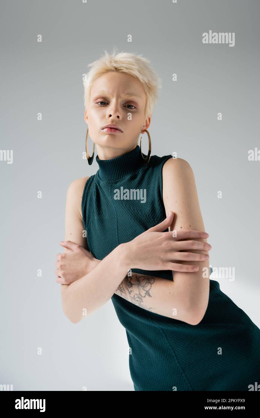 tattooed albino woman in tight dress embracing herself on grey background Stock Photo