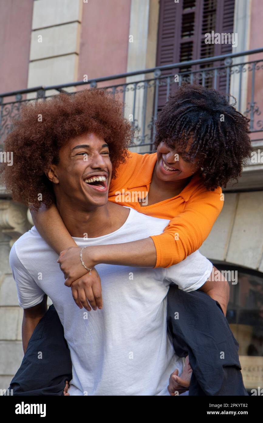 Cheerful African American male looking away while giving piggyback ride to  smiling black girlfriend with Afro hairstyle and walking on street in dayti  Stock Photo - Alamy