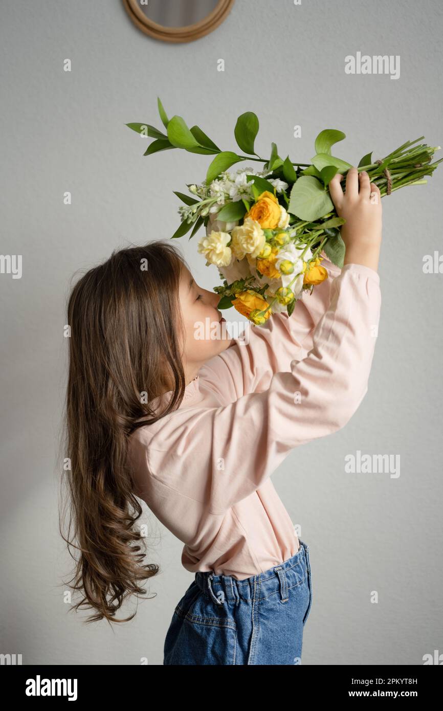 Side view of preteen girl with eyes closed smelling bouquet of flowers ...