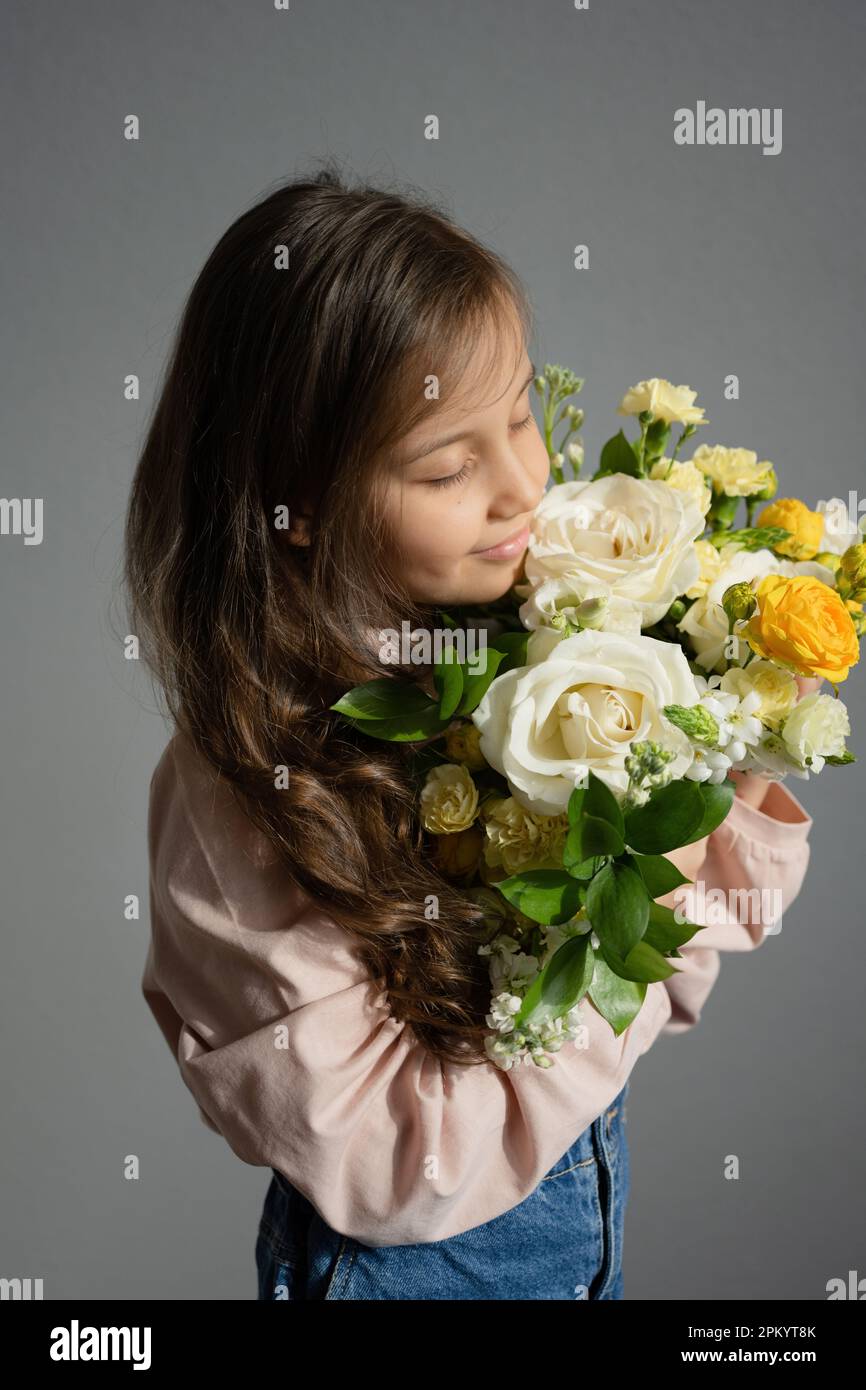 Side view of preteen girl with eyes closed smelling bouquet of flowers ...