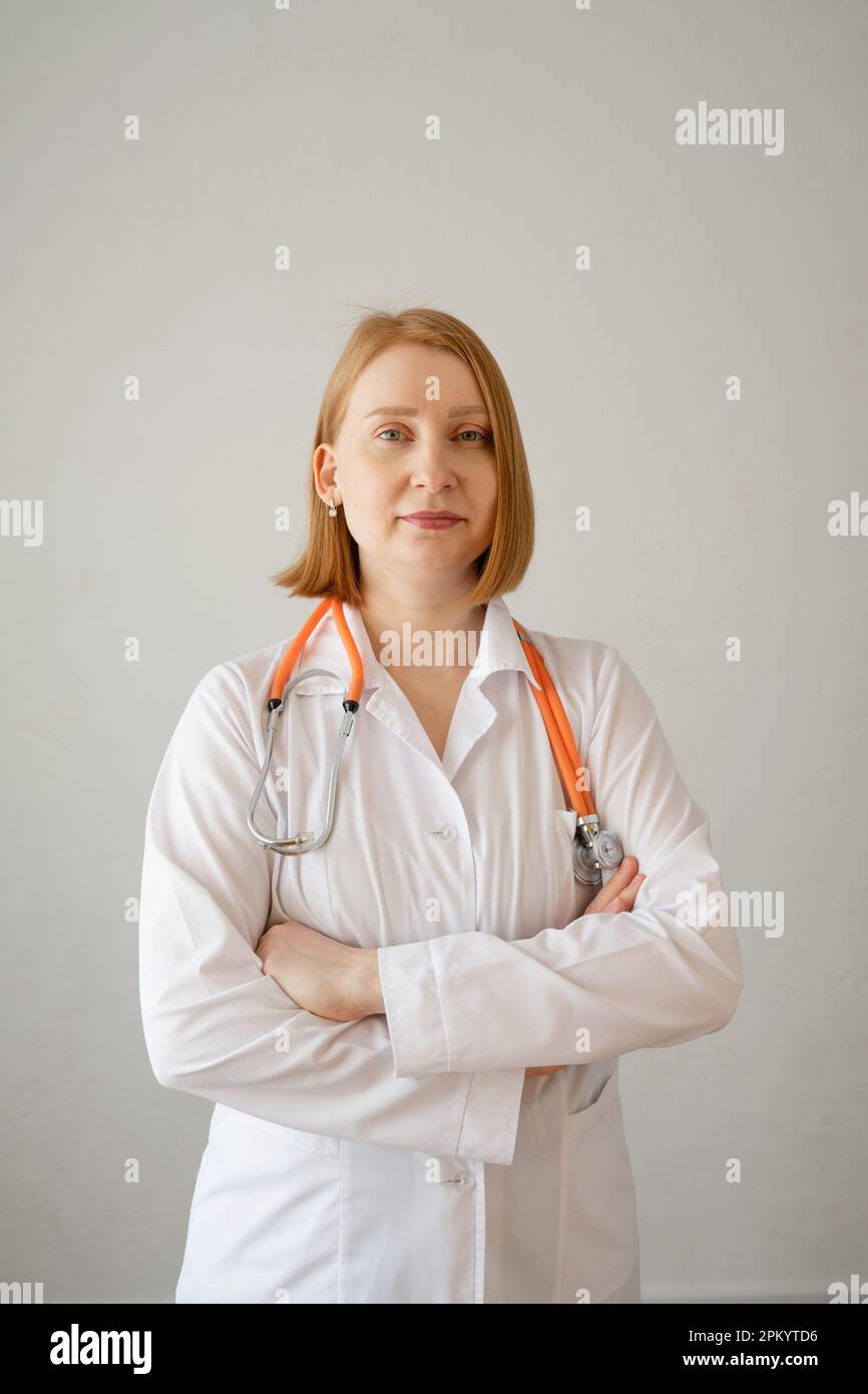 Smiling young female doctor in white coat using stethoscope and looking