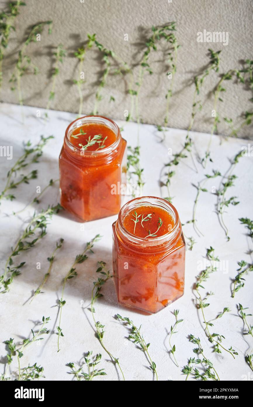 Jars filled with homemade fruit jam placed on table with green sprigs of thyme Stock Photo