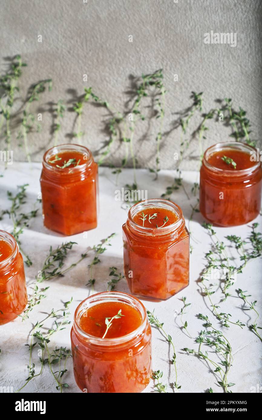 Jars filled with homemade fruit jam placed on table with green sprigs of thyme Stock Photo