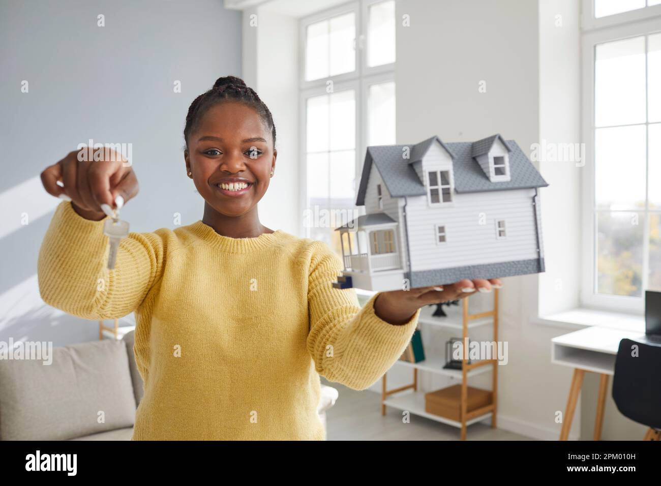 Portrait of a happy woman holding a house model and showing the key to ...