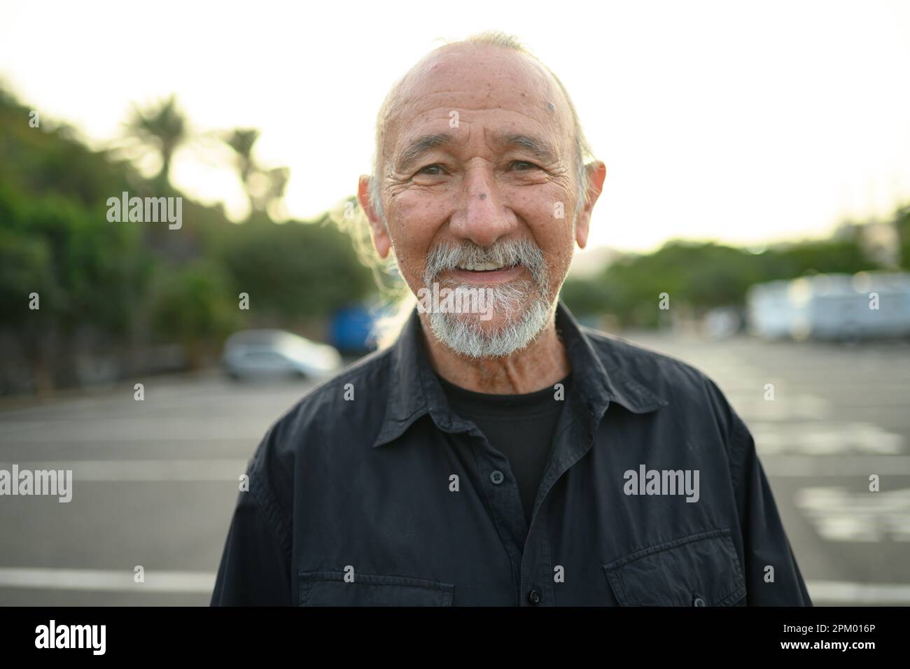 Portrait of smiling senior bearded male in casual clothes looking at camera while standing on blurred city street during daytime Stock Photo