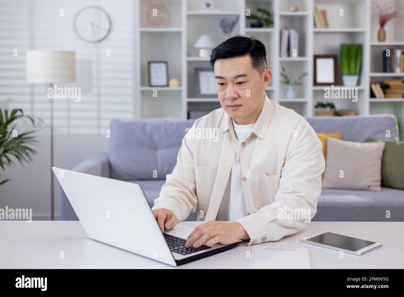 Serious and focused Asian man, businessman, freelancer, student working studying at home using laptop, Sitting at table and talking on video call, typing. Stock Photo