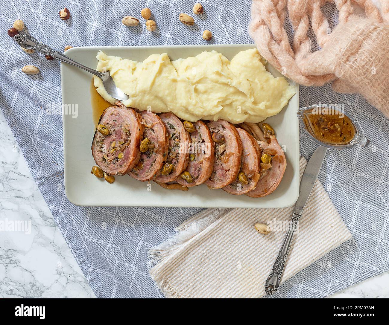 A plate with some silces of filled pork and mashed potatoes. At side: a wool scarf and a glass sauce boat. Stock Photo