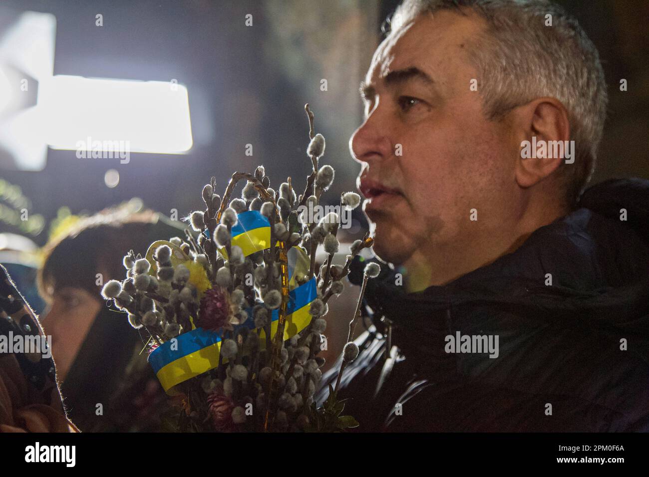 KYIV, UKRAINE - APRIL 9, 2023 - A man holds willow branches tied with a ribbon in the colours of the Ukrainian flag during the divine liturgy at the R Stock Photo