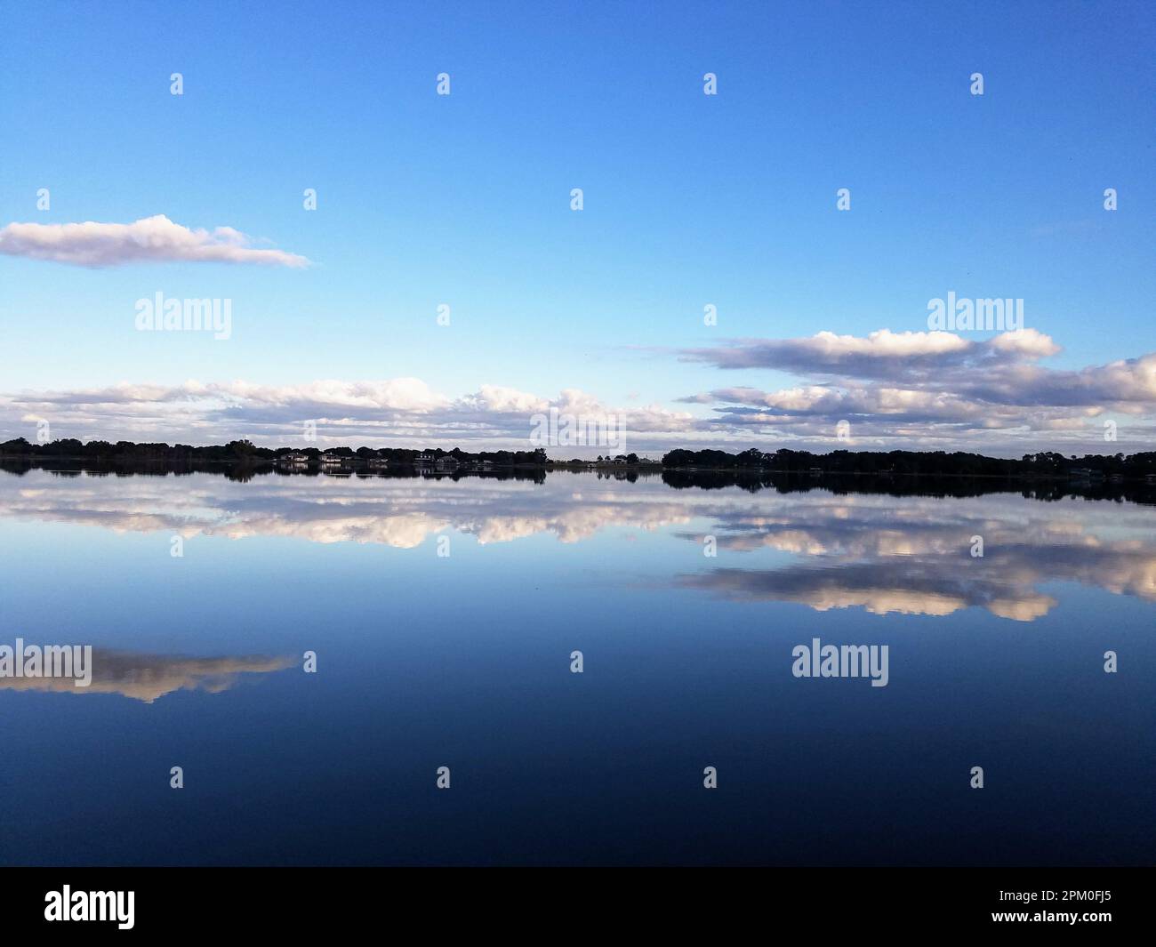 A tranquil lake reflecting the bright blue sky with white clouds Stock ...