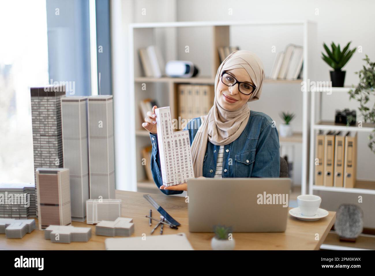 Smiling muslim lady in hijab posing with architectural model in front ...