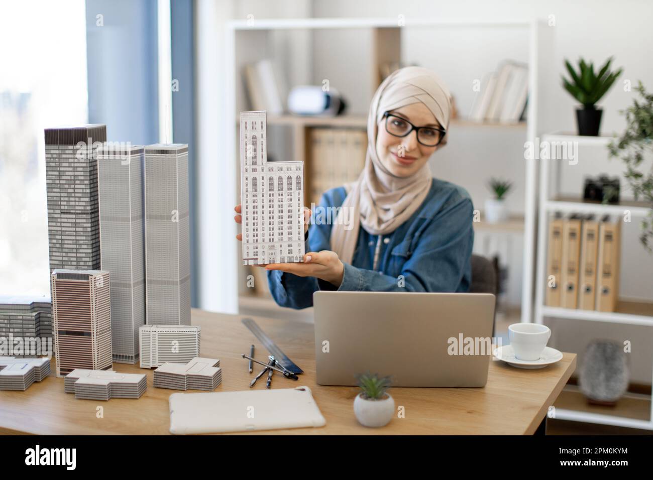 Smiling muslim lady in hijab posing with architectural model in front ...
