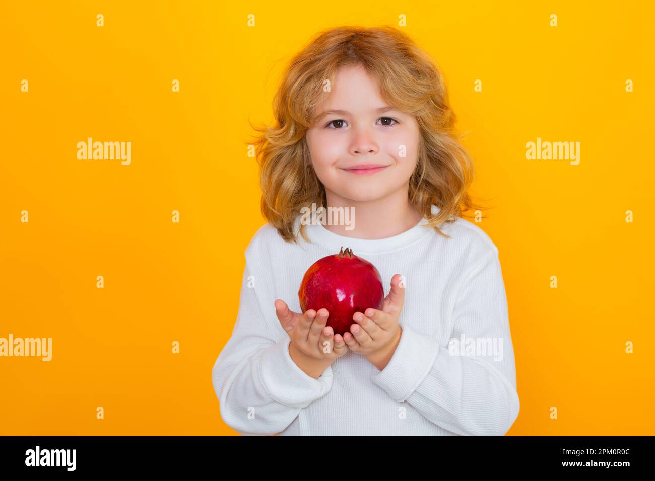 Healthy fruits for kids. Kid hold red pomegranate in studio. Pomegranate fruit. Studio portrait of cute child with pomegranate isolated on yellow back Stock Photo