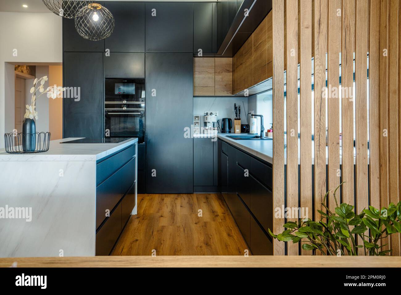 A modern kitchen with a combination of black cabinets, white marble and ...