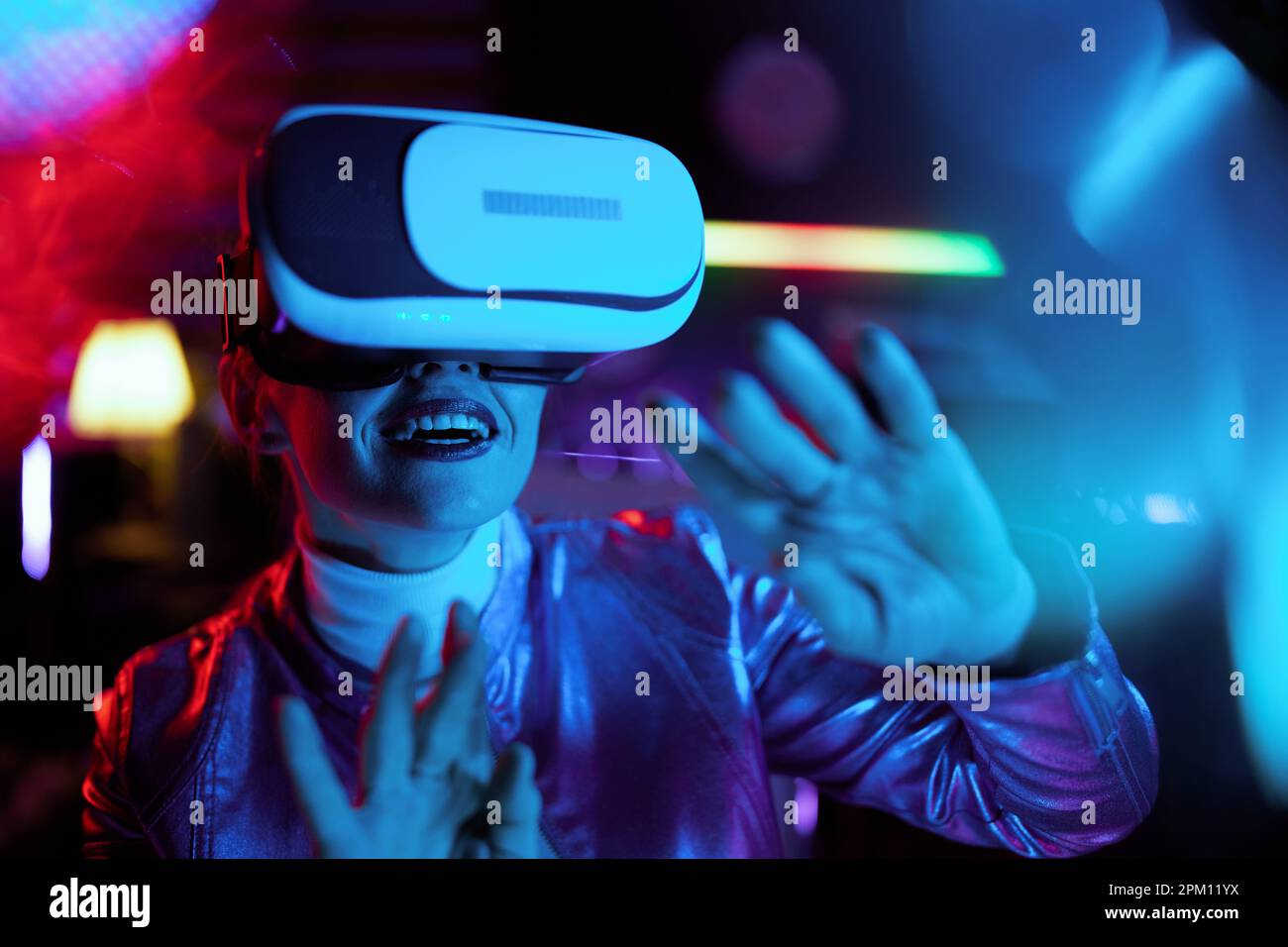 Neon metaverse futuristic concept. smiling trendy 40 years old woman in vr headset designing virtual reality. Stock Photo