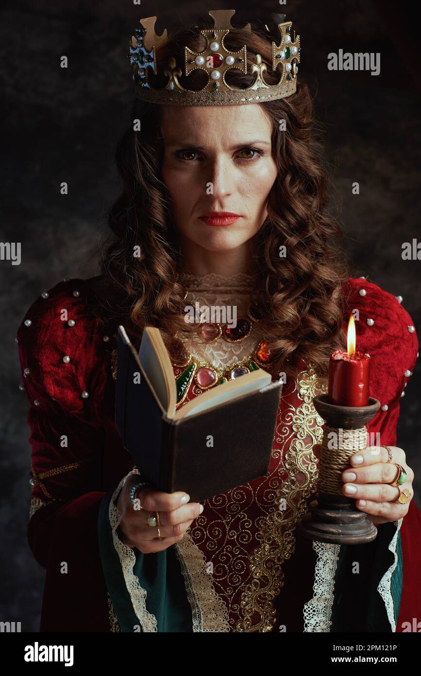medieval queen in red dress with book, candle and crown on dark gray ...