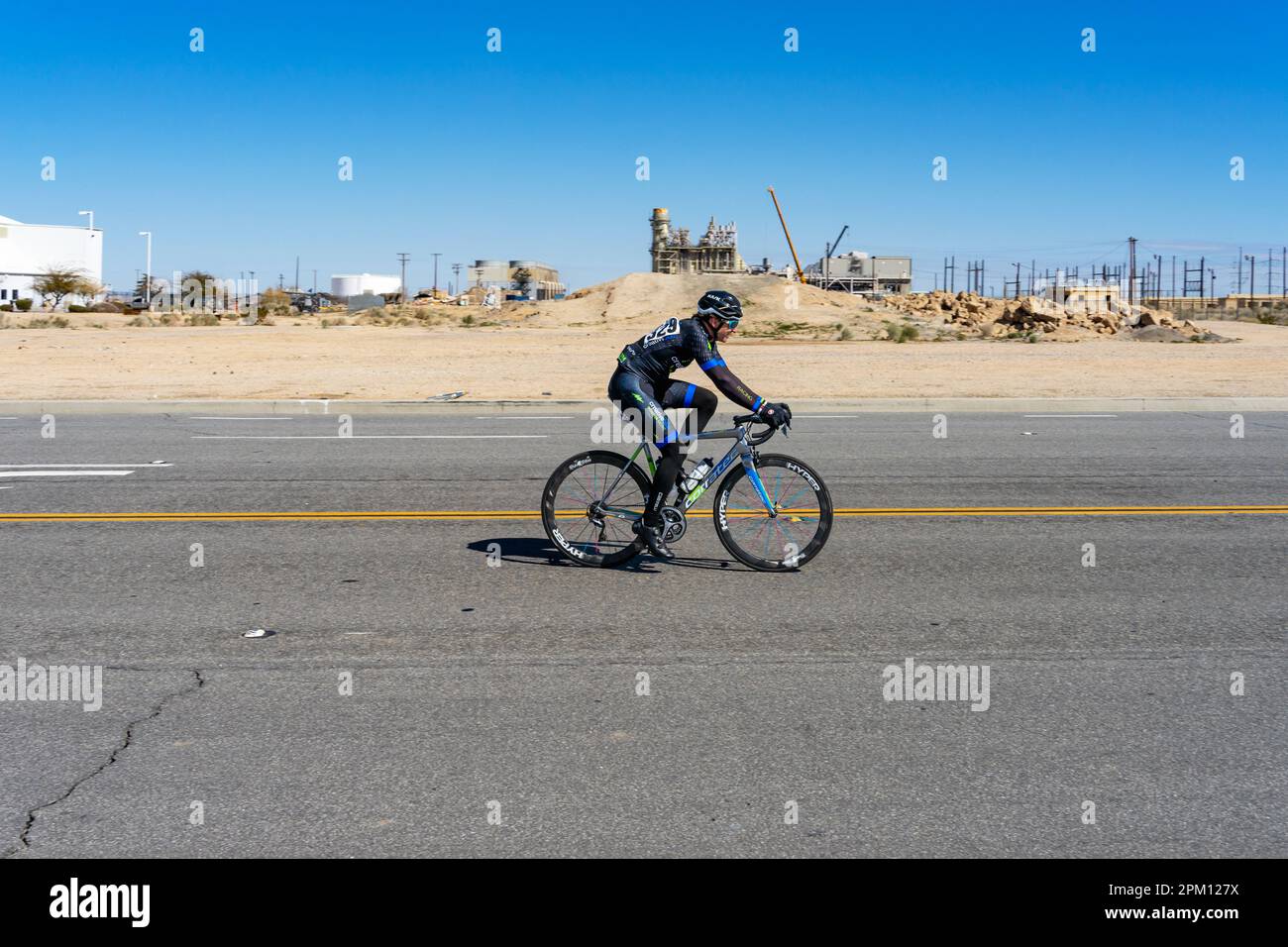 Victorville, CA, USA – March 25, 2023: A male cyclist rides pass an industrial area during a cycling road race in Victorville, California. Stock Photo