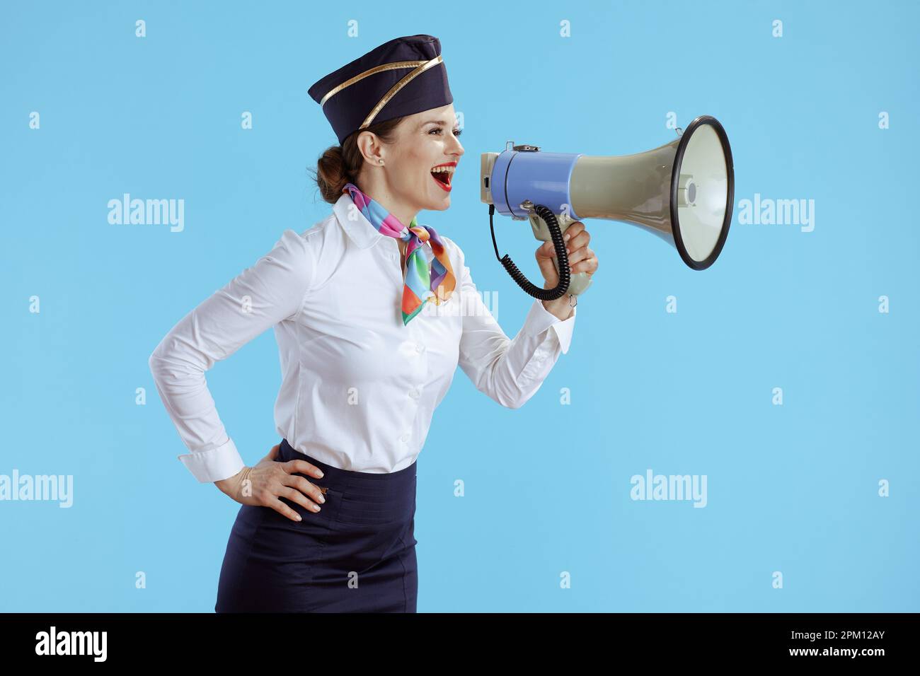 smiling elegant air hostess woman on blue background in uniform with megaphone. Stock Photo