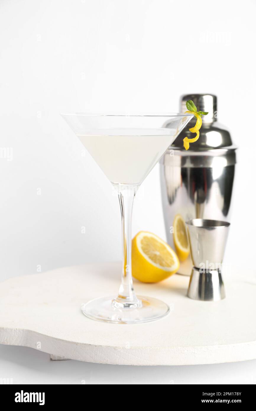 Glass of tasty martini, jigger, shaker and lemon on white background