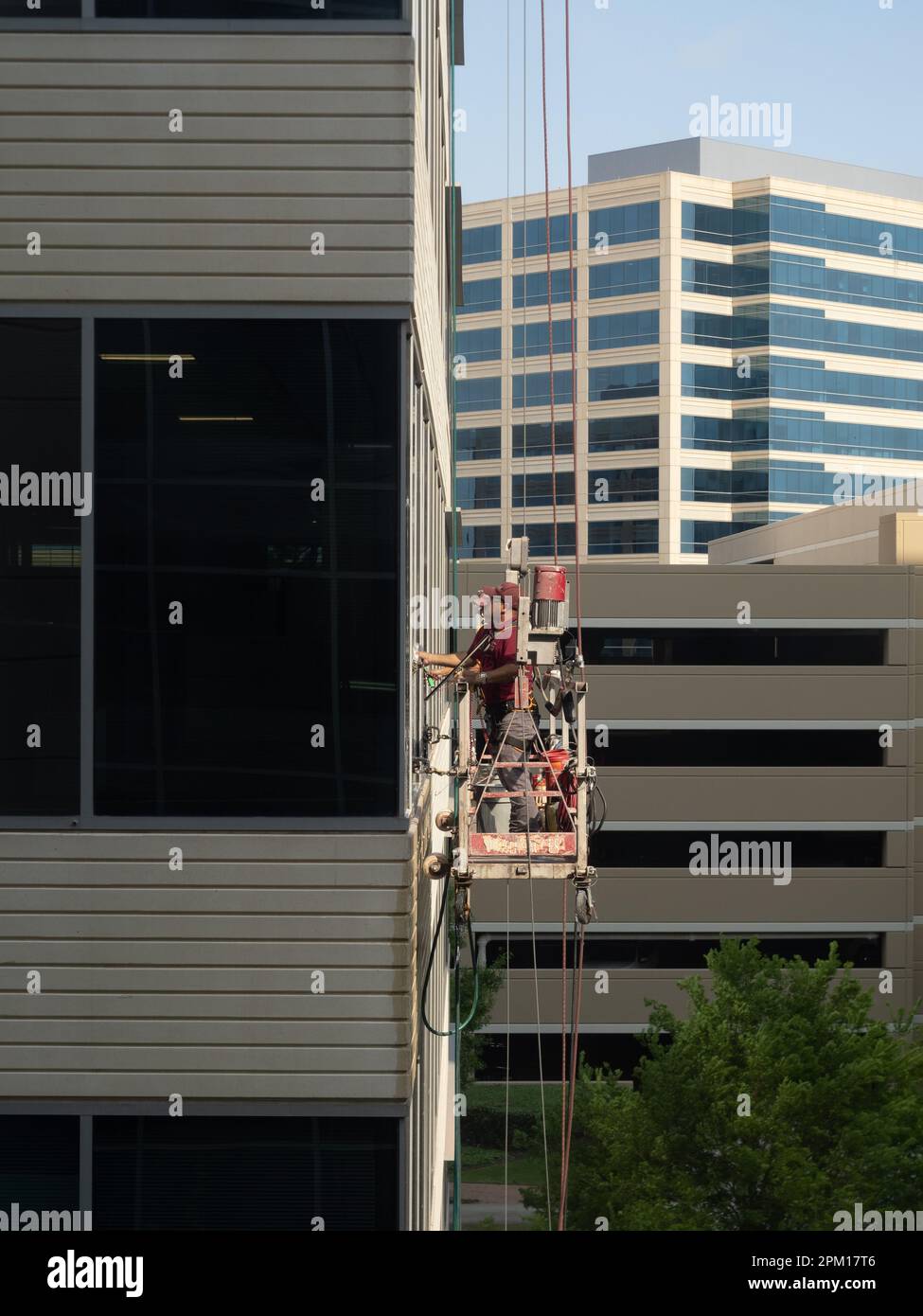 Eye level view of two male uniformed window washers cleaning glass on an office building while standing on a suspended scaffold. Stock Photo