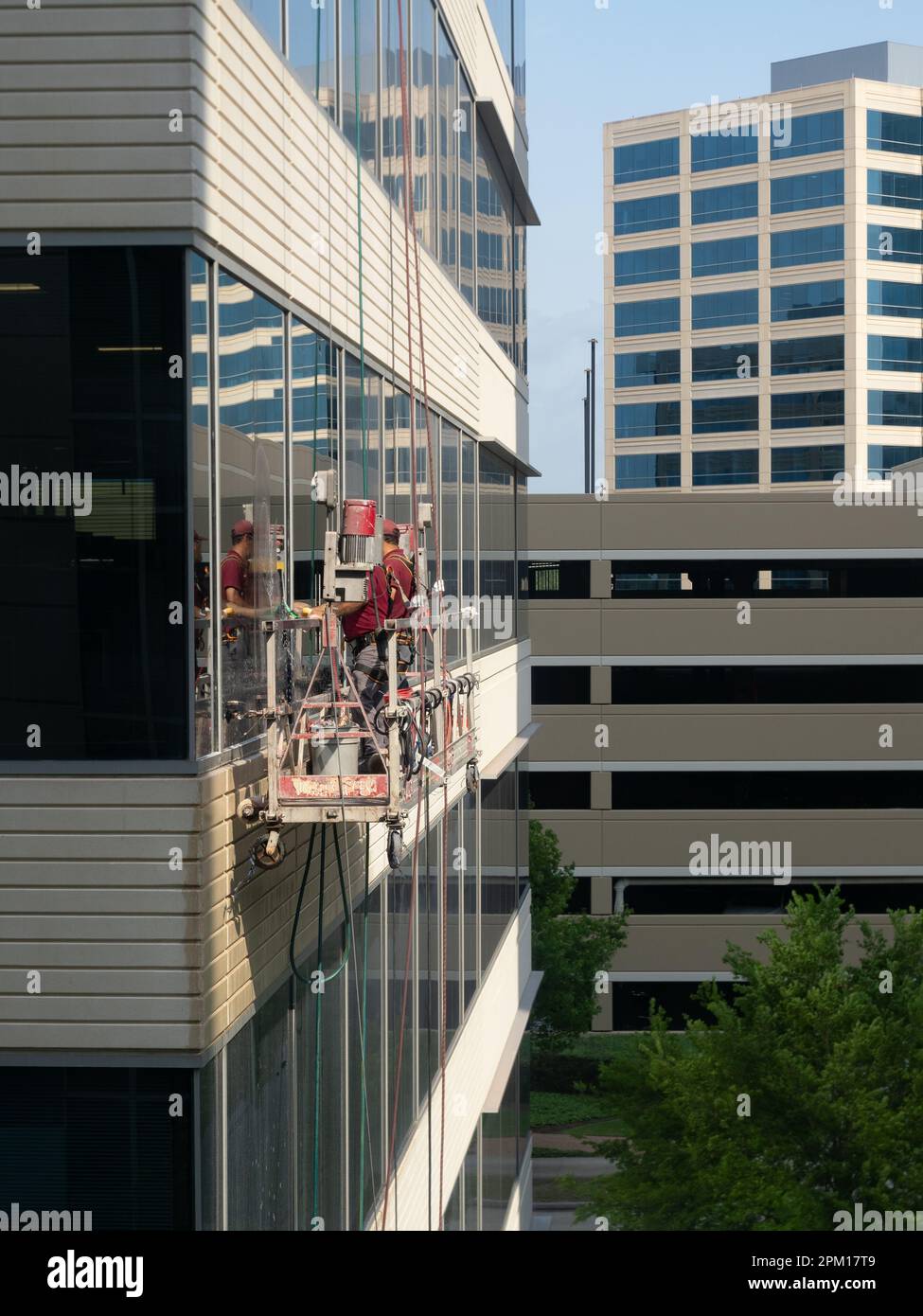 Close up of two male window washers standing on a suspended scaffold while washing glass on an office building, Photographed at eye level. Stock Photo